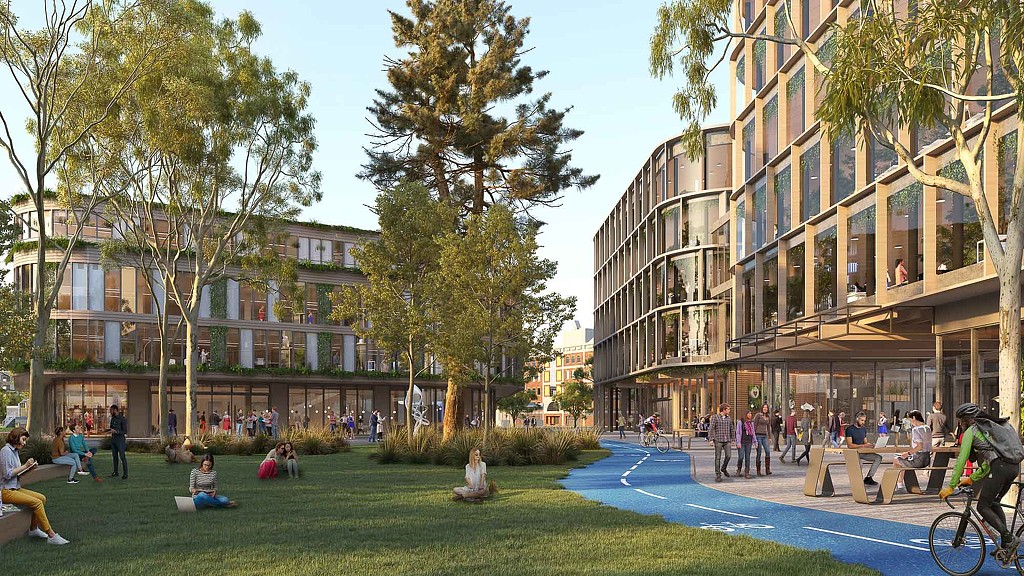 A group of people sitting on the grass by a building.